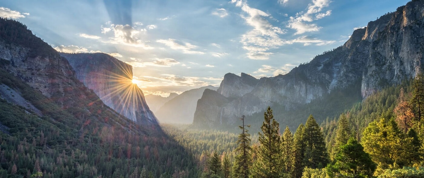 Lever de soleil spectaculaire sur la vallée de Yosemite avec rayons lumineux, forêts de conifères et falaises granitiques